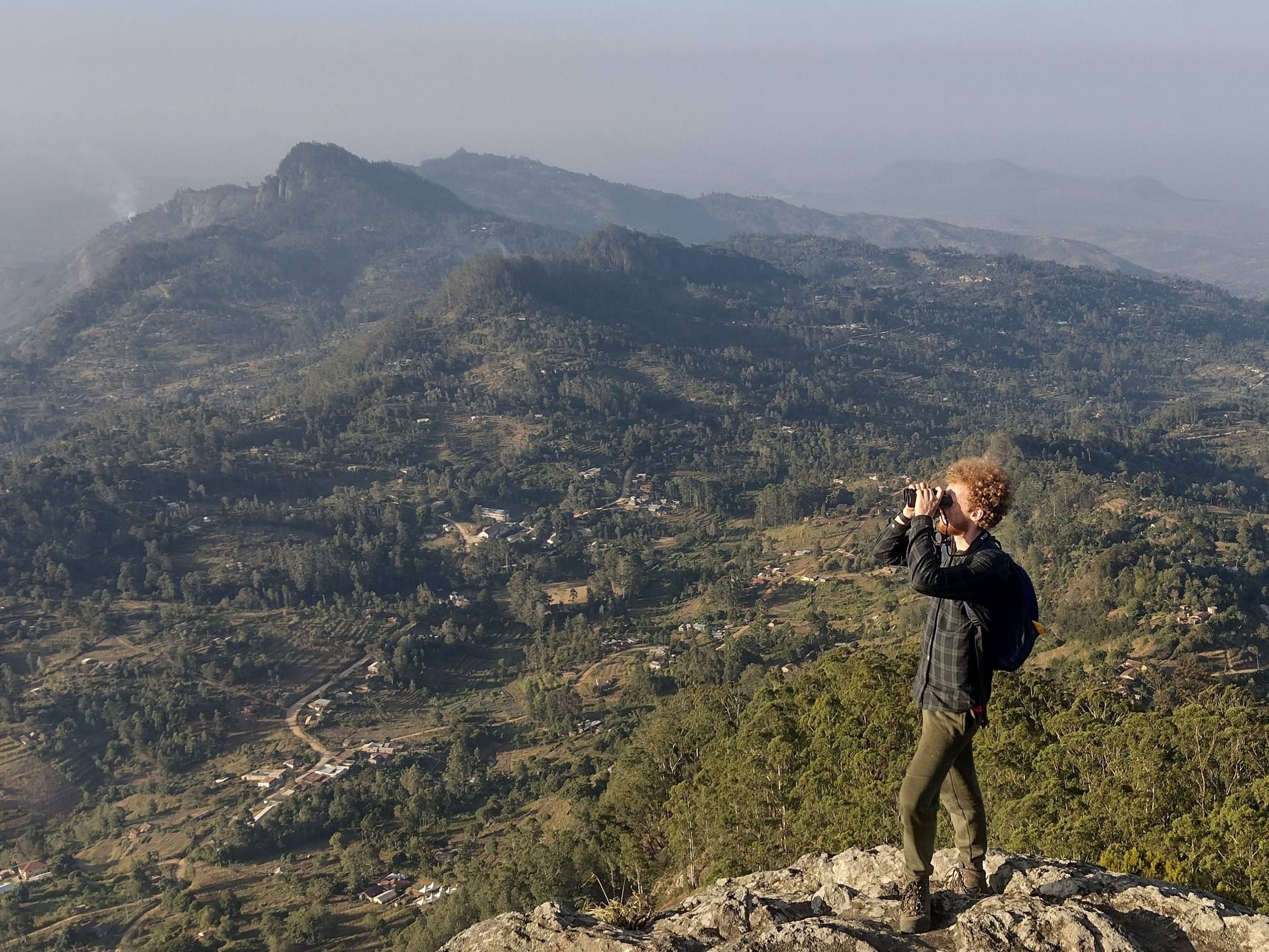 Liam De Bosscher looking through binoculars over forested hills